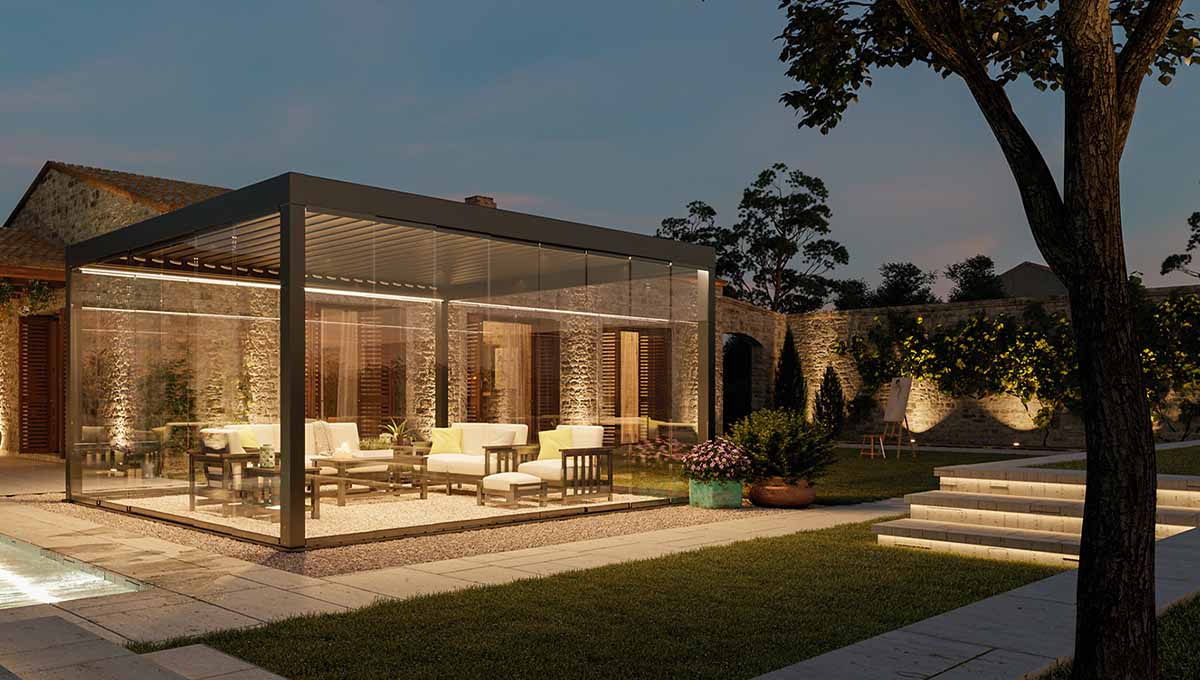 pergola bioclimatique essential éclairée sur terrasse contre façade de maison ancienne de nuit